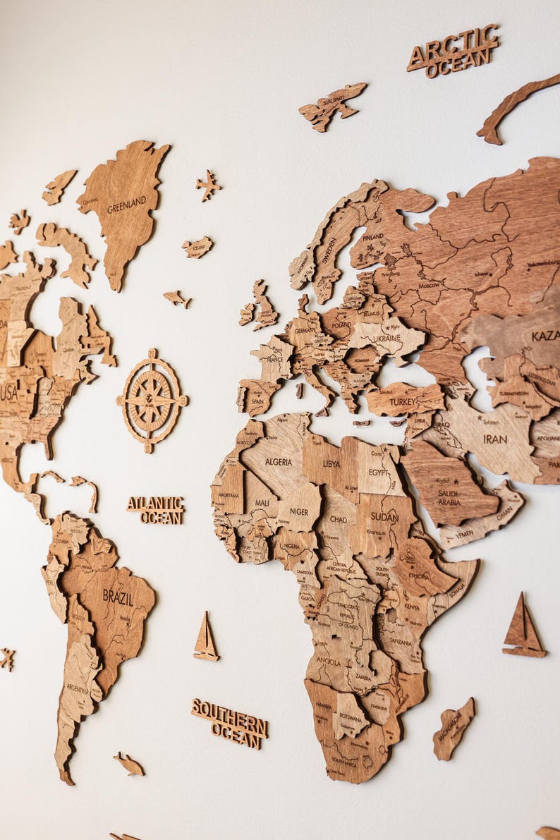 Pode incluir: Um mapa-m&uacute;ndi de madeira com contornos detalhados de pa&iacute;ses, incluindo EUA, Brasil e Gronel&acirc;ndia. O mapa apresenta r&oacute;tulos oce&acirc;nicos como "Oceano Atl&acirc;ntico" e "Oceano &Aacute;rtico". Velas decorativas de madeira e uma rosa dos ventos tamb&eacute;m est&atilde;o inclu&iacute;das.