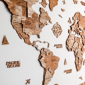 Pode incluir: Um mapa-m&uacute;ndi de madeira com contornos detalhados de pa&iacute;ses e r&oacute;tulos de oceanos. O mapa apresenta uma rosa dos ventos e pequenos detalhes de madeira, como avi&otilde;es e veleiros. O mapa &eacute; feito de madeira marrom clara.
