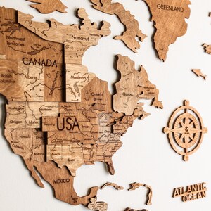 Pode incluir: Um mapa-m&uacute;ndi de madeira com contornos detalhados de pa&iacute;ses, incluindo EUA, Canad&aacute; e M&eacute;xico. O mapa &eacute; feito de madeira marrom clara e inclui o Oceano Atl&acirc;ntico e a Groenl&acirc;ndia. Uma rosa dos ventos tamb&eacute;m est&aacute; inclu&iacute;da.