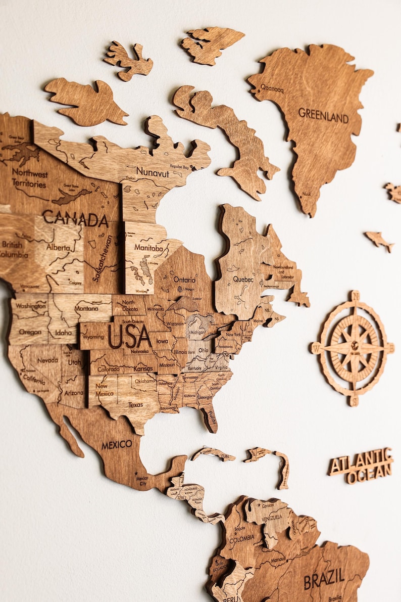 Pode incluir: Um mapa-m&uacute;ndi de madeira com contornos detalhados de pa&iacute;ses, incluindo EUA, Canad&aacute; e M&eacute;xico. O mapa &eacute; feito de madeira marrom clara e inclui o Oceano Atl&acirc;ntico e a Groenl&acirc;ndia. Uma rosa dos ventos tamb&eacute;m est&aacute; inclu&iacute;da.