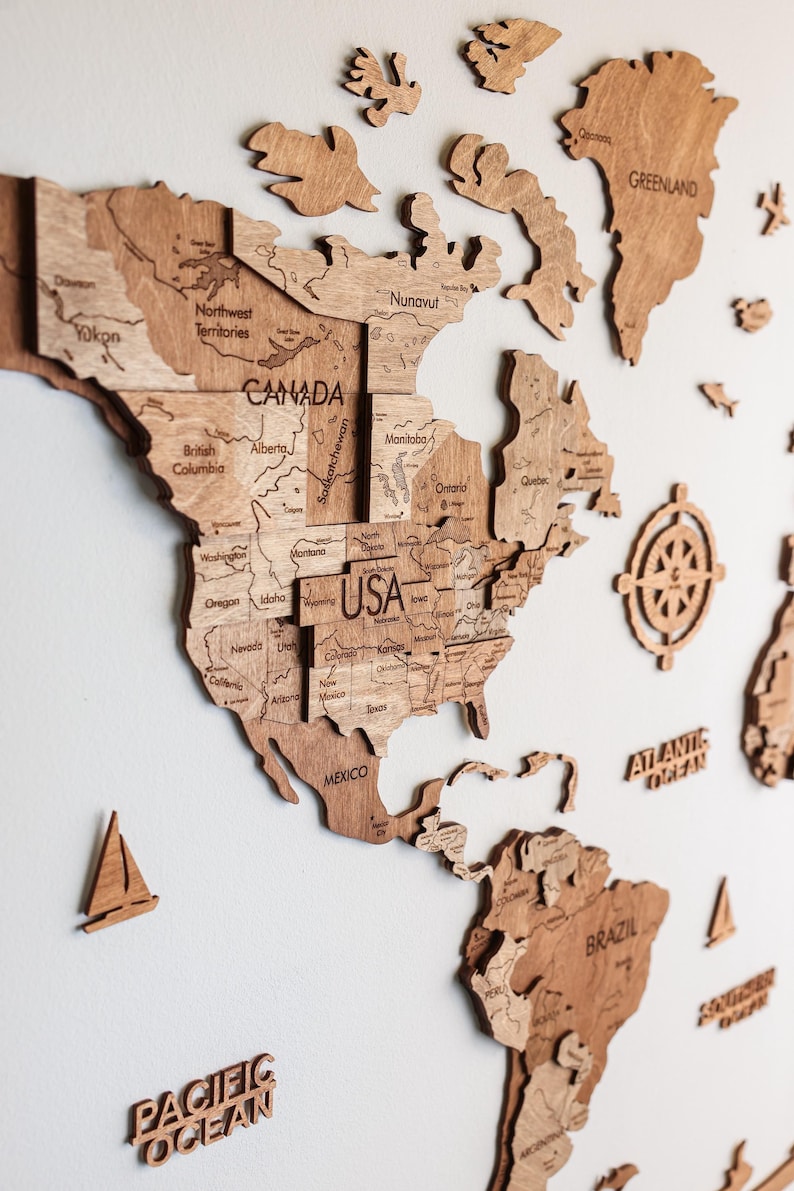 Pode incluir: Um mapa-m&uacute;ndi de madeira com contornos detalhados de pa&iacute;ses, incluindo EUA, Canad&aacute; e M&eacute;xico. O mapa &eacute; feito de madeira castanha clara e inclui pe&ccedil;as separadas para continentes e ilhas. Elementos decorativos como uma b&uacute;ssola e veleiros tamb&eacute;m est&atilde;o presentes.
