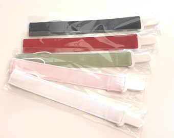 May include: Five fabric headbands in various colors: navy, red, olive green, pink, and white. Each headband is packaged in a clear plastic sleeve with a white cardboard backing. The headbands are flat and rectangular.