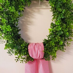 May include: A green leafy wreath with a red and white striped bow.