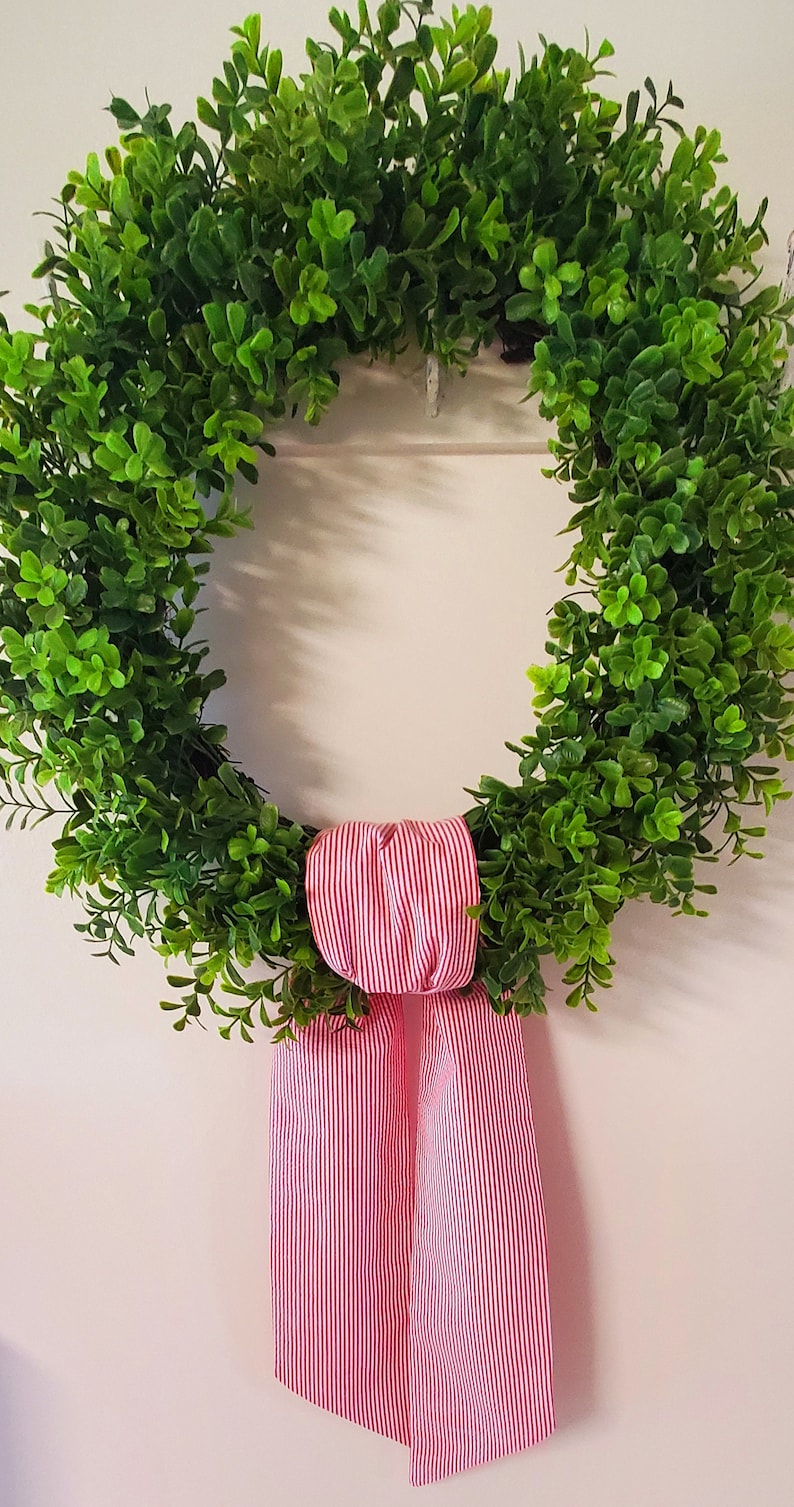 May include: A green leafy wreath with a red and white striped bow.