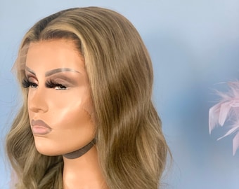 May include: A long, wavy, light brown wig with blonde highlights. The wig is styled in loose waves and falls to the shoulders.