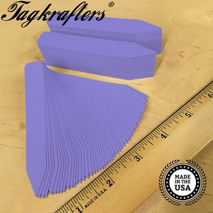 May include: A stack of 100 lavender plant markers, made in the USA. The markers are approximately 3 inches long and have a pointed end. The markers are arranged in a fan shape and are being measured with a ruler.