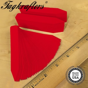 May include: A stack of 50 bright red plastic plant markers with pointed ends. The markers are arranged in a fan shape and are next to a wooden ruler. The ruler is marked with inches and has the text "MADE IN U.S.A." printed on it. A round sticker with the text "MADE IN THE USA" is visible in the lower right corner of the image.