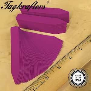 May include: A stack of 50 bright magenta plastic plant markers with pointed ends. The markers are arranged in a fan shape and measure approximately 3 inches in length. The markers are made in the USA.