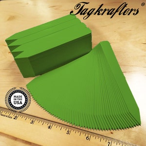 May include: A stack of 100 green plant markers with pointed ends. The markers are made in the USA. The markers are arranged in a fan shape and are next to a ruler.