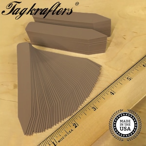 May include: Stacks of brown plant tags with a pointed end, fanned out on a wooden surface. The brand name "Tagkrafers" is visible in the top left corner. A wooden ruler with inch measurements is in the background. The words "Made in the USA" are in a circular emblem.