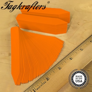 May include: A stack of 50 bright orange plant markers with pointed ends. The markers are 3 inches long and are made in the USA.  The markers are arranged in a fan shape and are next to a wooden ruler.