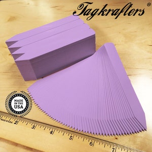 May include: A stack of 100 lavender plant markers, made in the USA. The markers are 2 inches long and have a pointed end. They are arranged in a fan shape, with the pointed ends facing out. The markers are made of a durable plastic material and are perfect for labeling plants in your garden.
