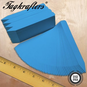 May include: A stack of 100 blue plastic plant markers, each measuring 2 inches long. The markers are arranged in a fan shape, with the tips pointing towards the right. A ruler is visible in the bottom left corner of the image. The text "Tagkraftlers" is visible in the top left corner of the image. The text "Made in the USA" is visible in the bottom right corner of the image.