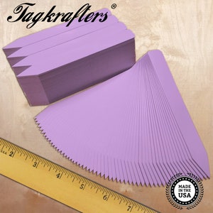 May include: A stack of light purple plant markers with a pointed top and a serrated edge. The brand name "Tagkrafers" is visible in the upper left corner. A wooden ruler is in the lower left corner, and a "Made in the USA" seal is in the lower right.