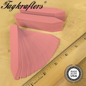 May include: A stack of 50 pink plant markers with pointed ends. The markers are arranged in a fan shape and measure approximately 2 inches in length. The markers are made in the USA.