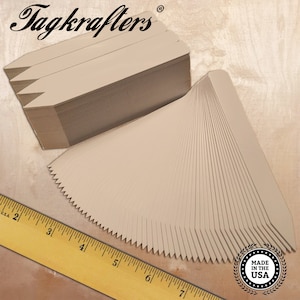May include: A stack of beige plant tags with a pointed top and a serrated edge. The tags are arranged in a fan shape, with the text "Tagkrafters" in the upper left corner. A ruler is in the lower left corner, and a "Made in the USA" seal is in the lower right.