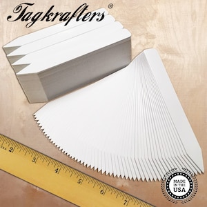May include: A stack of 100 white plant markers with pointed ends. The markers are approximately 2 inches long and are made in the USA.  The markers are arranged in a fan shape with a ruler in the foreground.