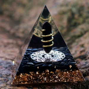 May include: A black obsidian pyramid with a gold-wrapped crystal point and a black and silver mandala design on the base. The pyramid is surrounded by black obsidian chips and gold flakes.
