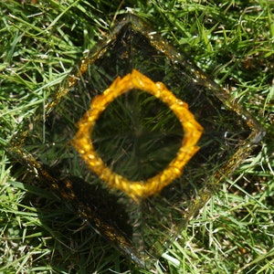 K&ouml;nnte beinhalten: Eine klare Glaspyramide mit einem goldenen Glitzerrand. Die Pyramide steht auf einem Bett aus gr&uuml;nem Gras.