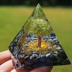 Pode incluir: Uma pirâmide de vidro transparente com uma árvore de aventurina verde dentro. A árvore tem um tronco de fio de cobre e está cercada por glitter dourado e pedras pretas.