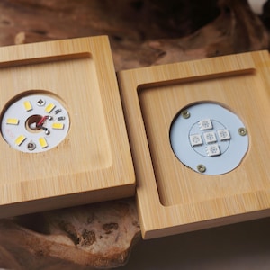 Könnte beinhalten: Zwei Holzkisten mit transparenten Kunststoffeinsätzen. Die Einsätze enthalten LED-Leuchten. Eine Kiste hat eine einzelne LED-Leuchte, während die andere mehrere LED-Leuchten hat.