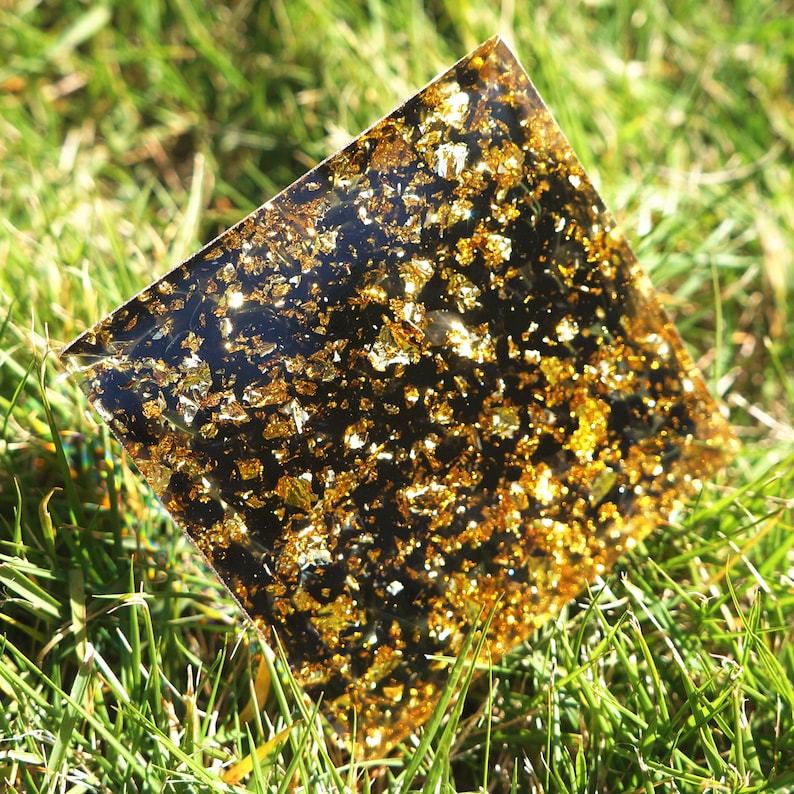 K&ouml;nnte beinhalten: Ein quadratisches St&uuml;ck durchsichtiges Harz mit eingebetteten goldenen Flocken. Das Harz liegt auf einem Bett aus gr&uuml;nem Gras.