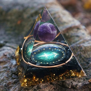 Peut inclure: Une pyramide en verre transparent avec une base verte et dorée, une sphère de cristal d'améthyste violette et un cercle bordé d'or avec un symbole zodiacal vert et or à l'intérieur.