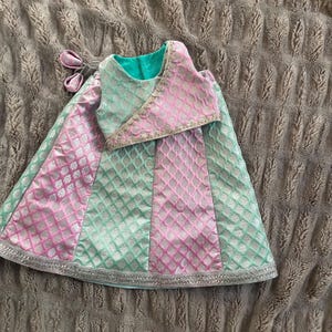 May include: A baby girl's outfit in pink and green with a geometric pattern. The outfit includes a skirt and a matching top.