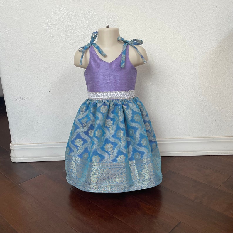 May include: A lavender sleeveless dress with a white lace waistband and a blue and silver patterned skirt.