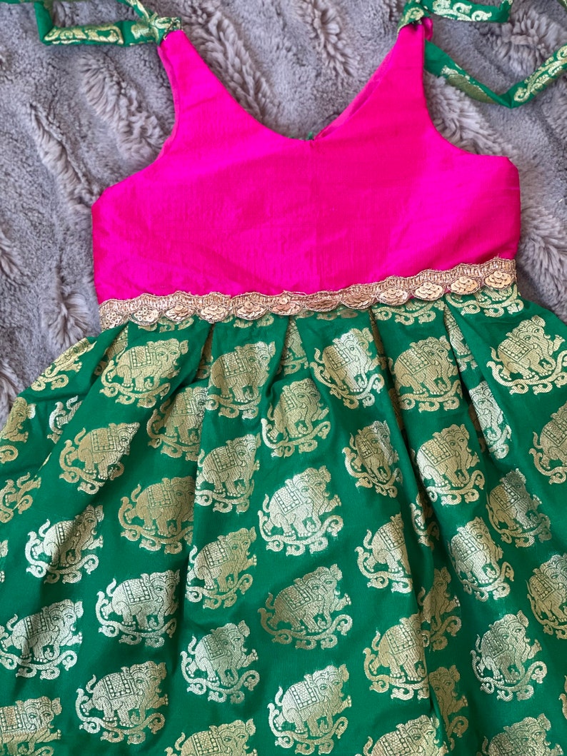 Puede incluir: Un vestido verde con un corpi&ntilde;o rosa y ribetes dorados. La falda tiene un patr&oacute;n de elefantes dorados sobre un fondo verde.