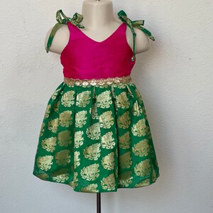 Puede incluir: Un vestido verde y rosa con ribete dorado y estampado de elefantes. El vestido tiene cuello en V y tirantes de lazo.