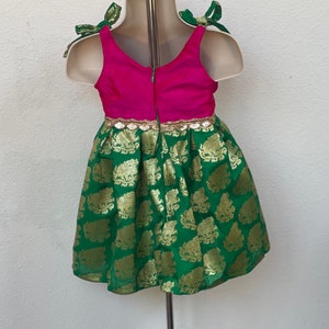Puede incluir: Un vestido verde y rosa con detalles dorados y una cremallera en la espalda. El vestido tiene una falda verde con un estampado de elefantes dorados y un corpi&ntilde;o rosa con ribetes dorados. El vestido tiene tirantes verdes que se atan en lazos.