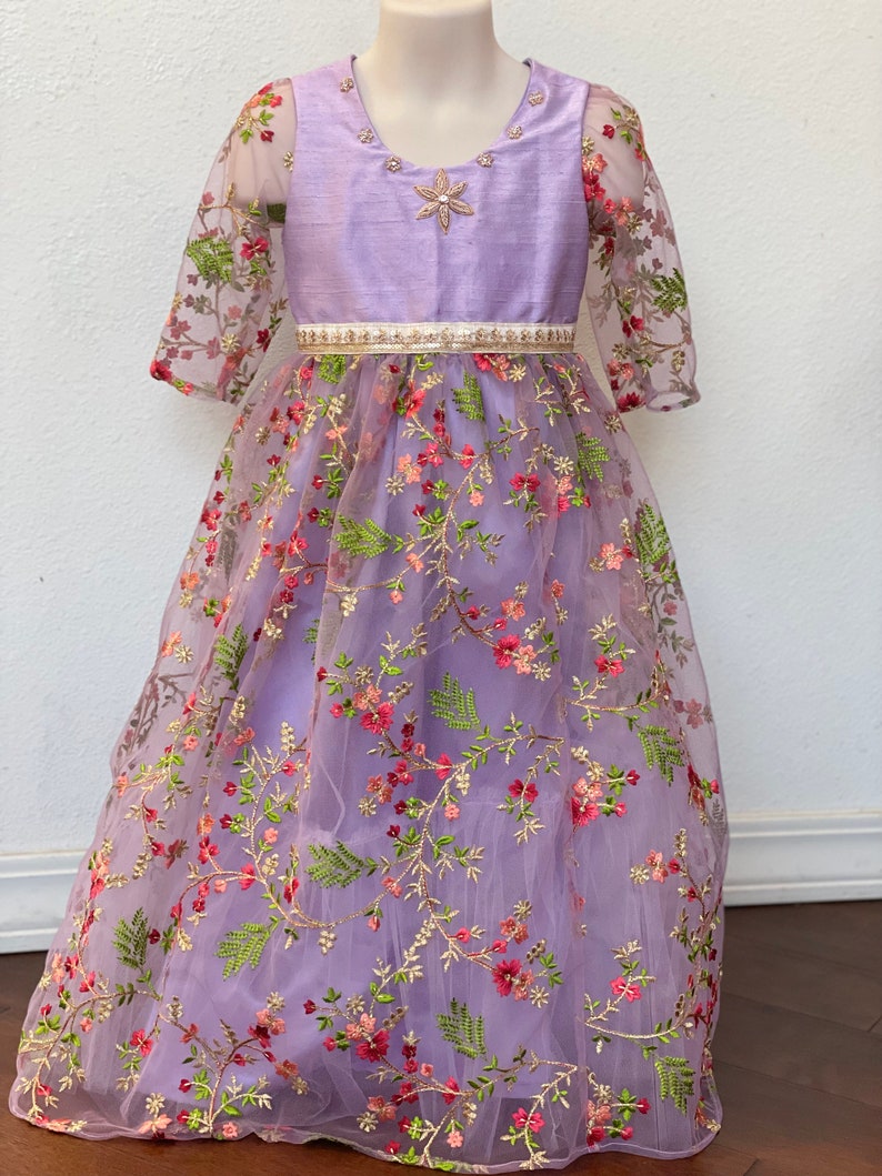 May include: A lavender dress with a floral embroidered tulle overlay. The dress has a satin bodice with a beaded neckline and a white satin belt.