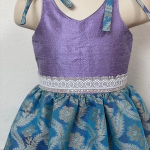 May include: A purple sleeveless dress with a white lace trim and a blue and gold patterned skirt.
