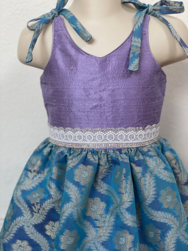 May include: A purple sleeveless dress with a white lace trim and a blue and gold patterned skirt.