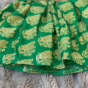 Puede incluir: Una falda verde con estampado de elefantes dorados y un corpi&ntilde;o rosa. La falda tiene un ribete dorado alrededor del borde inferior.