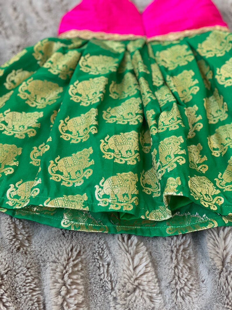 Puede incluir: Una falda verde con estampado de elefantes dorados y un corpi&ntilde;o rosa. La falda tiene un ribete dorado alrededor del borde inferior.