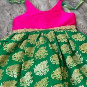 Puede incluir: Un vestido sin mangas verde y rosa con ribete dorado y estampado de elefantes. El vestido tiene un corpi&ntilde;o rosa y una falda verde con elefantes dorados.