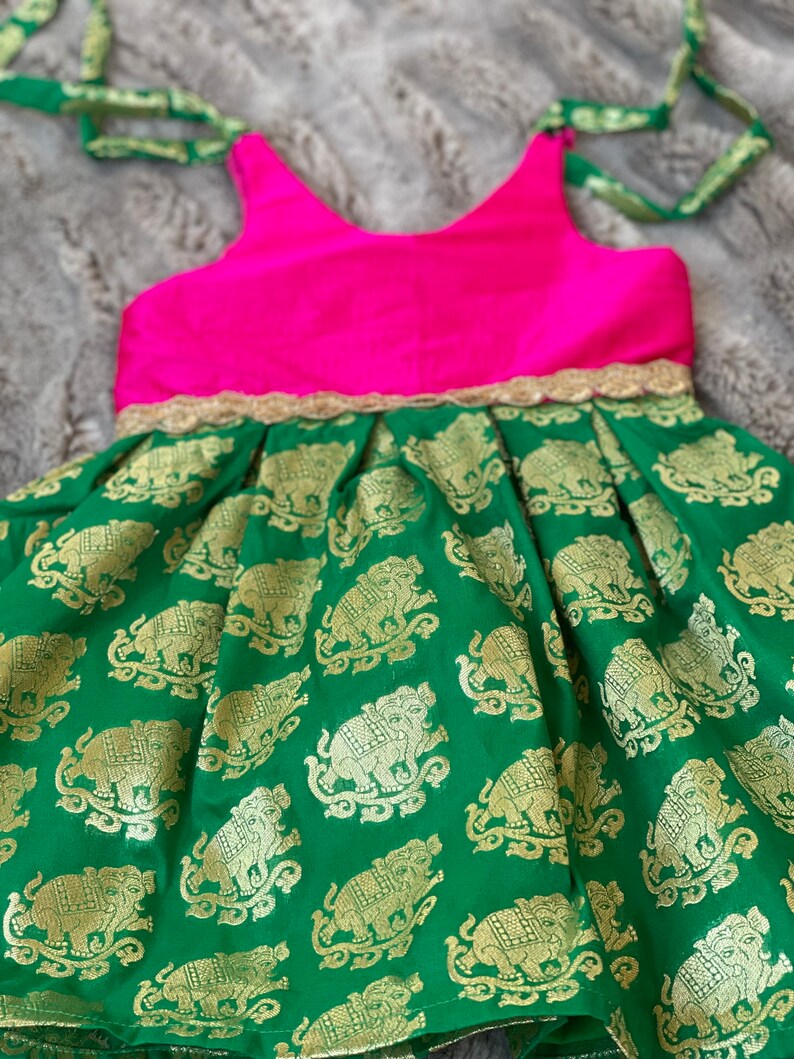 Puede incluir: Un vestido sin mangas verde y rosa con ribete dorado y estampado de elefantes. El vestido tiene un corpi&ntilde;o rosa y una falda verde con elefantes dorados.