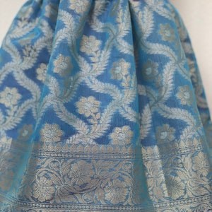 May include: A light blue skirt with a silver floral pattern. The skirt has a white lace waistband and a silver trim around the bottom.