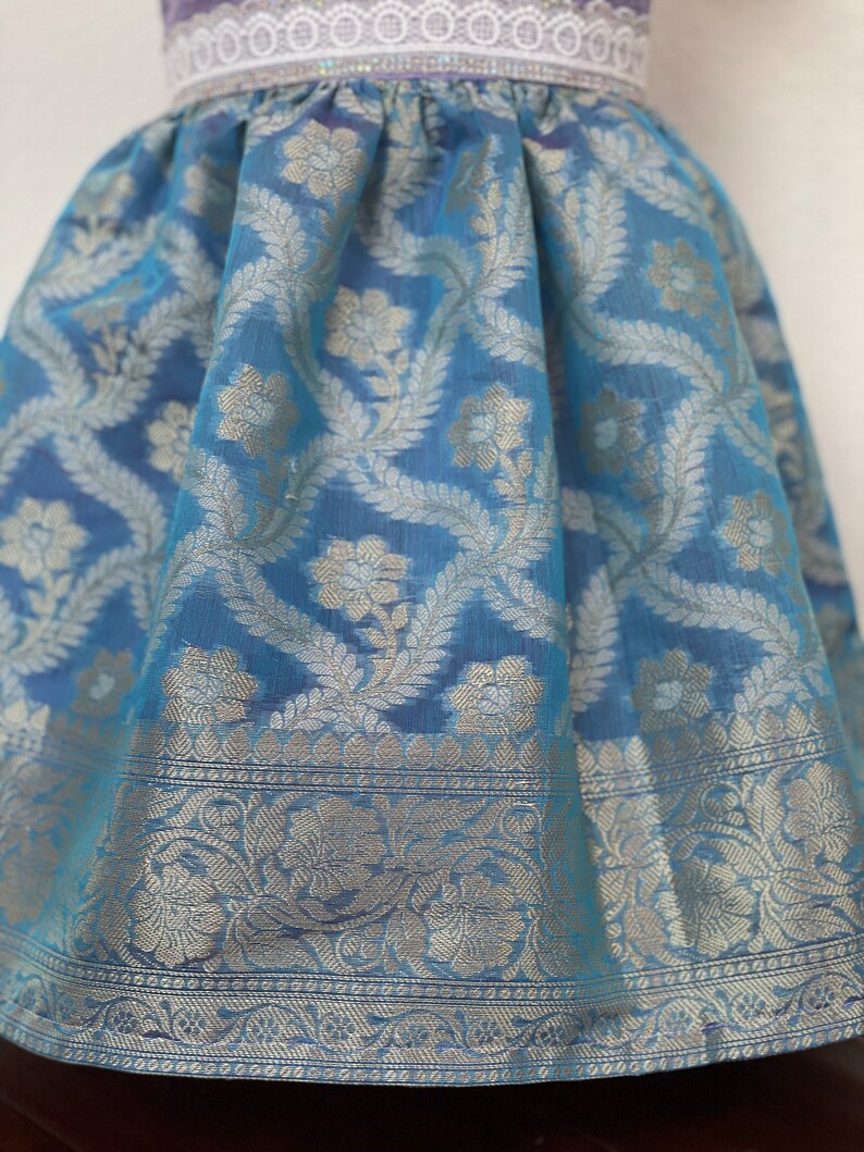May include: A light blue skirt with a silver floral pattern. The skirt has a white lace waistband and a silver trim around the bottom.