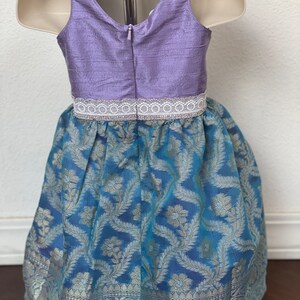 May include: A sleeveless dress with a lavender bodice and a blue and silver patterned skirt. The bodice has a white lace trim and a zipper in the back.