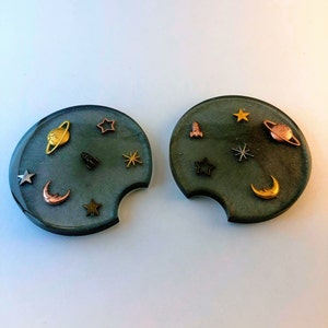 Peut inclure: Deux dessous-de-verre ronds de couleur vert foncé avec un morceau enlevé sur le côté. Chaque dessous-de-verre est décoré d'étoiles, de planètes, de fusées et de lunes dorées, argentées et cuivrées.