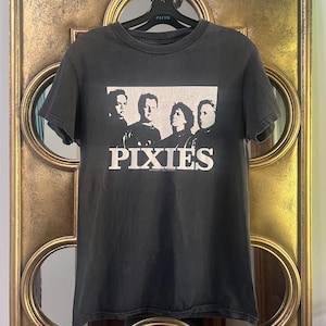 Puede incluir: Camiseta gris oscuro con una foto de la banda y la palabra "PIXIES" en blanco. La camiseta tiene cuello redondo y mangas cortas. La foto de la banda tiene forma rectangular.