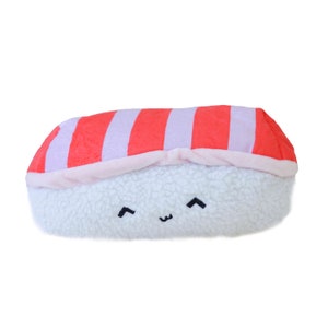 May include: A plush toy shaped like a sushi roll with a pink and red striped top and a white fluffy bottom. The toy has a cute smiling face with black eyes.