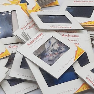 May include: A stack of vintage Kodachrome slides, some with the text "Kodachrome Transparency" printed on them. The slides are in various colours and have a faded look.