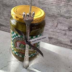 May include: A glass jar of Tony Packo's Pickles & Peppers with a silver fork bent into a middle finger shape, labeled "Fickle Pickle Poker".