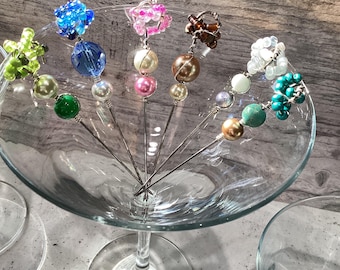 Könnte beinhalten: Ein Set mit zehn Cocktailrührern mit verschiedenen farbigen Glasperlen und Perlen. Die Rührer sind in einem Martini-Glas angeordnet.