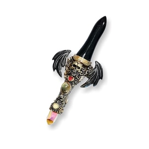 May include: A black dagger with a skull and wings design. The handle is decorated with gold and gemstones.
