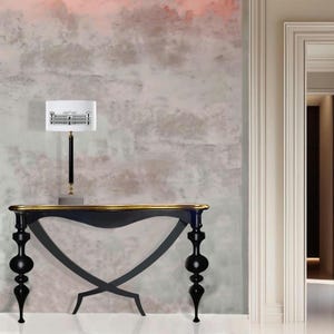 Può includere: Un tavolo console nero con un piano dorato e gambe nere ornate. Il tavolo è davanti a un muro con una carta da parati testurizzata rosa e grigia.